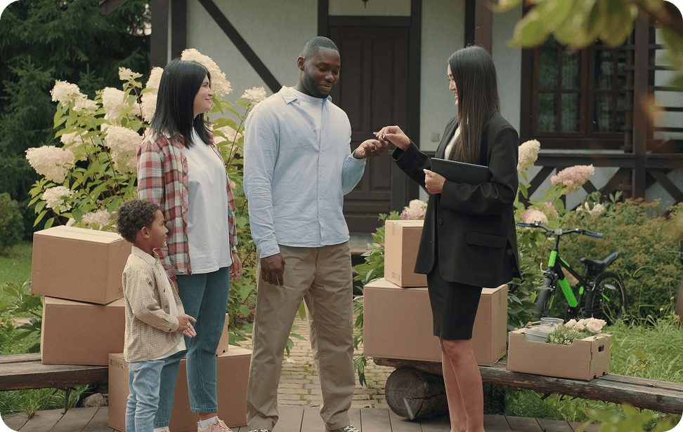 A family stands in front of a house surrounded by moving boxes, smiling and ready for their new beginning.