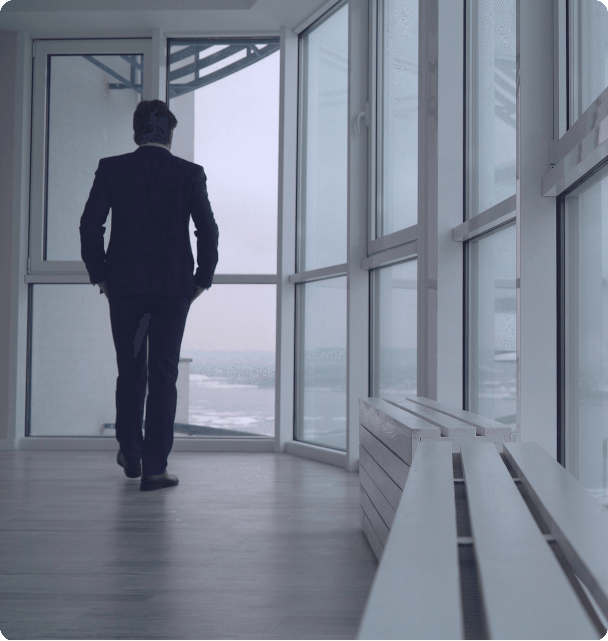 A well-dressed man stands by a large window, showcasing a professional demeanor in a bright, airy environment.