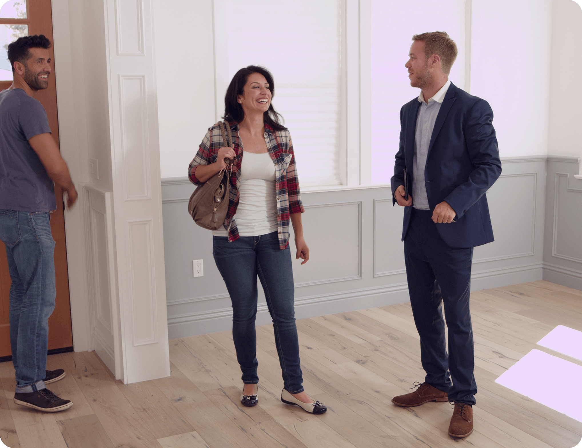 A man and woman stand in a room with a suited man, engaged in conversation.